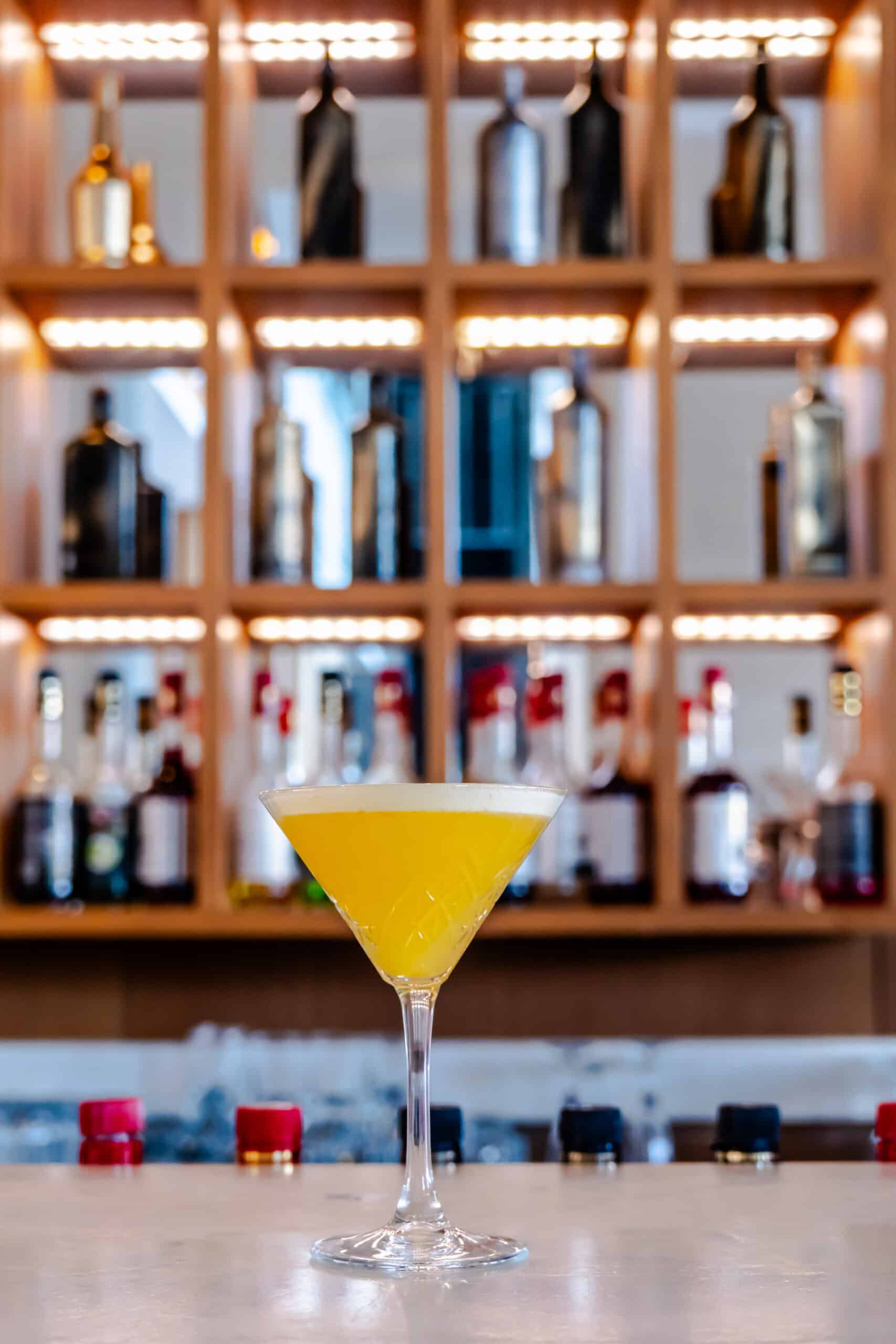 Sarı kokteyl, şişeler arkasında.