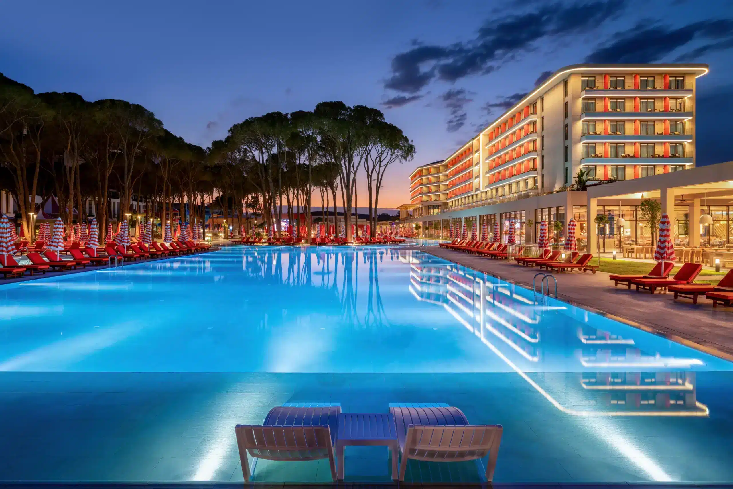 Abendansicht des Hauptpools, des fünfstöckigen Hauptgebäudes und der Pinien im Trendy Perge Resort & Suites
